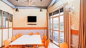 A conference room with a large table and orange chairs, a flat-screen TV on the wall, and large windows with curtains. - Vishen Residency (Greater Noida)