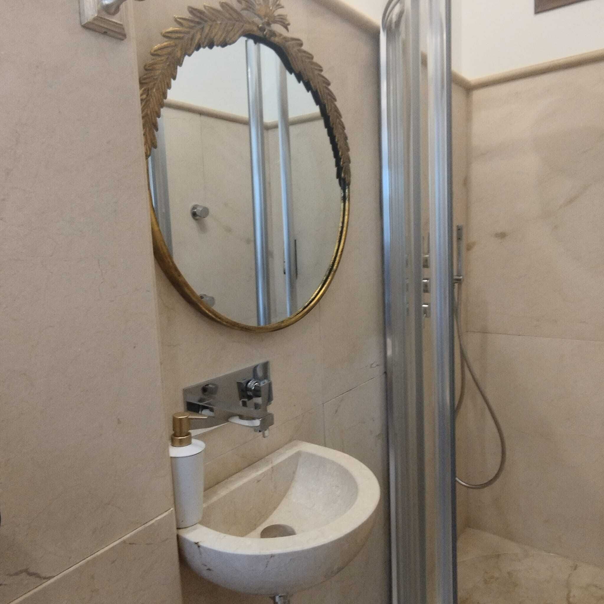 Un baño con lavamanos pedestal, espejo con marco decorativo y cabina de ducha.