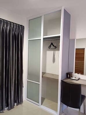 Una habitación con un armario corredero, una silla negra, una mesita y una percha para colgar ropa.