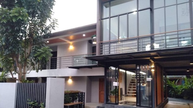 A modern building with a glass entrance, a covered outdoor seating area, and a staircase leading to an upper level.