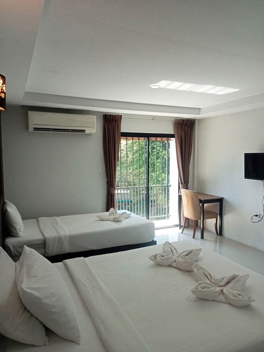 A hotel room with two beds, a desk, a chair, a TV, and a balcony with curtains.