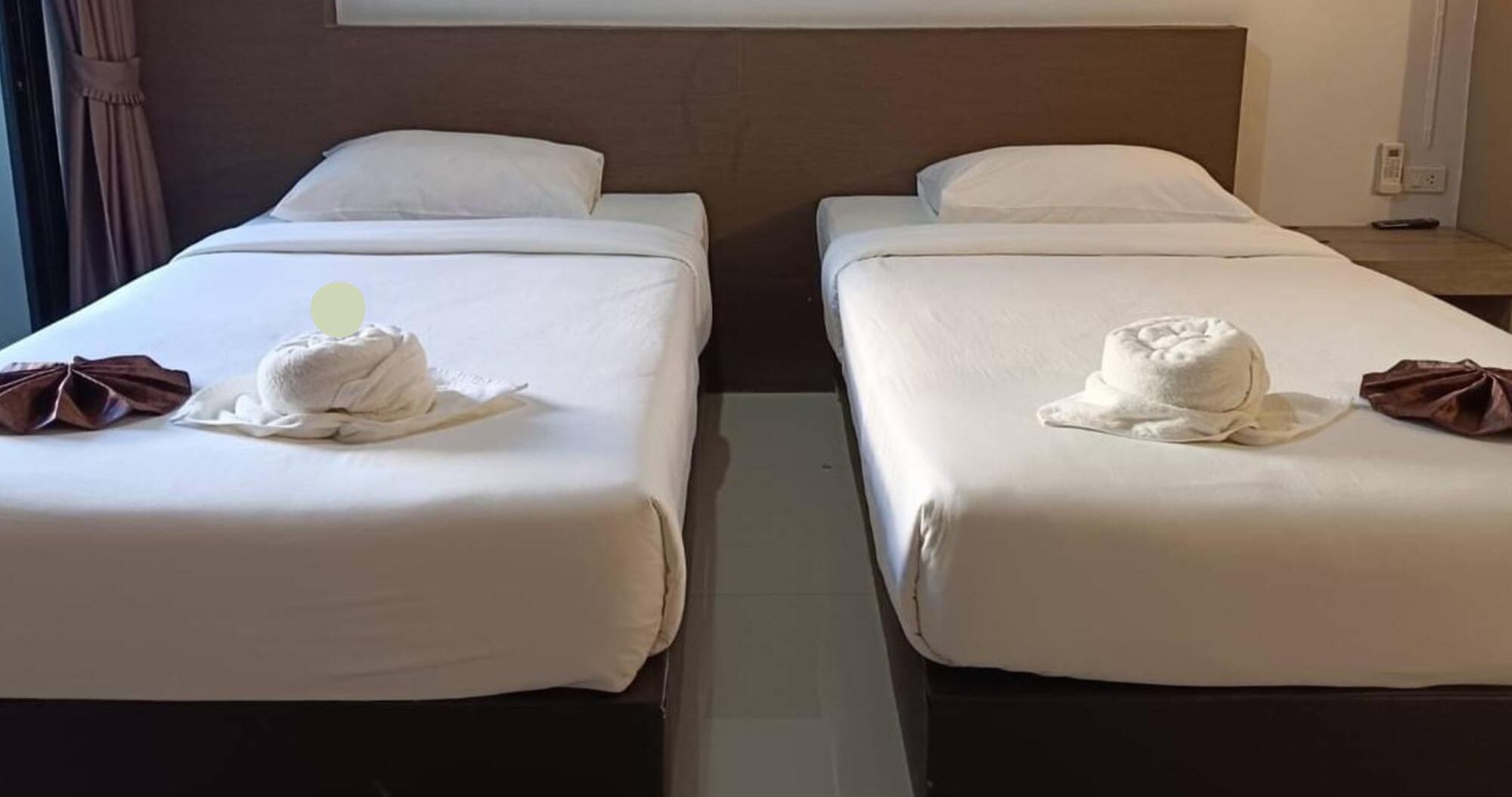 Two single beds with white linens and towels, a wooden headboard, and a small bedside table with a lamp.