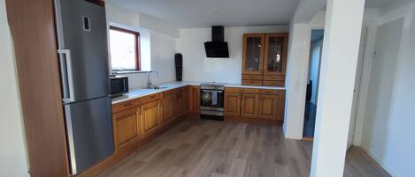 A kitchen with wooden cabinets, a stainless steel refrigerator, a microwave, a stove, and a black range hood.