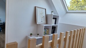 Ein Zimmer mit schrägem Dach, einem Holzzaun, einem Bücherregal und einem gerahmten Bild.