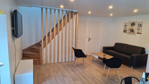 Ein modernes Wohnzimmer mit einer Holztreppe, einem schwarzen Sofa, zwei schwarzen Sesseln und einem kleinen Tisch.