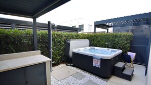 Un bain à remous installé sous une terrasse couverte, avec un espace salon, une petite table et un marchepied.
