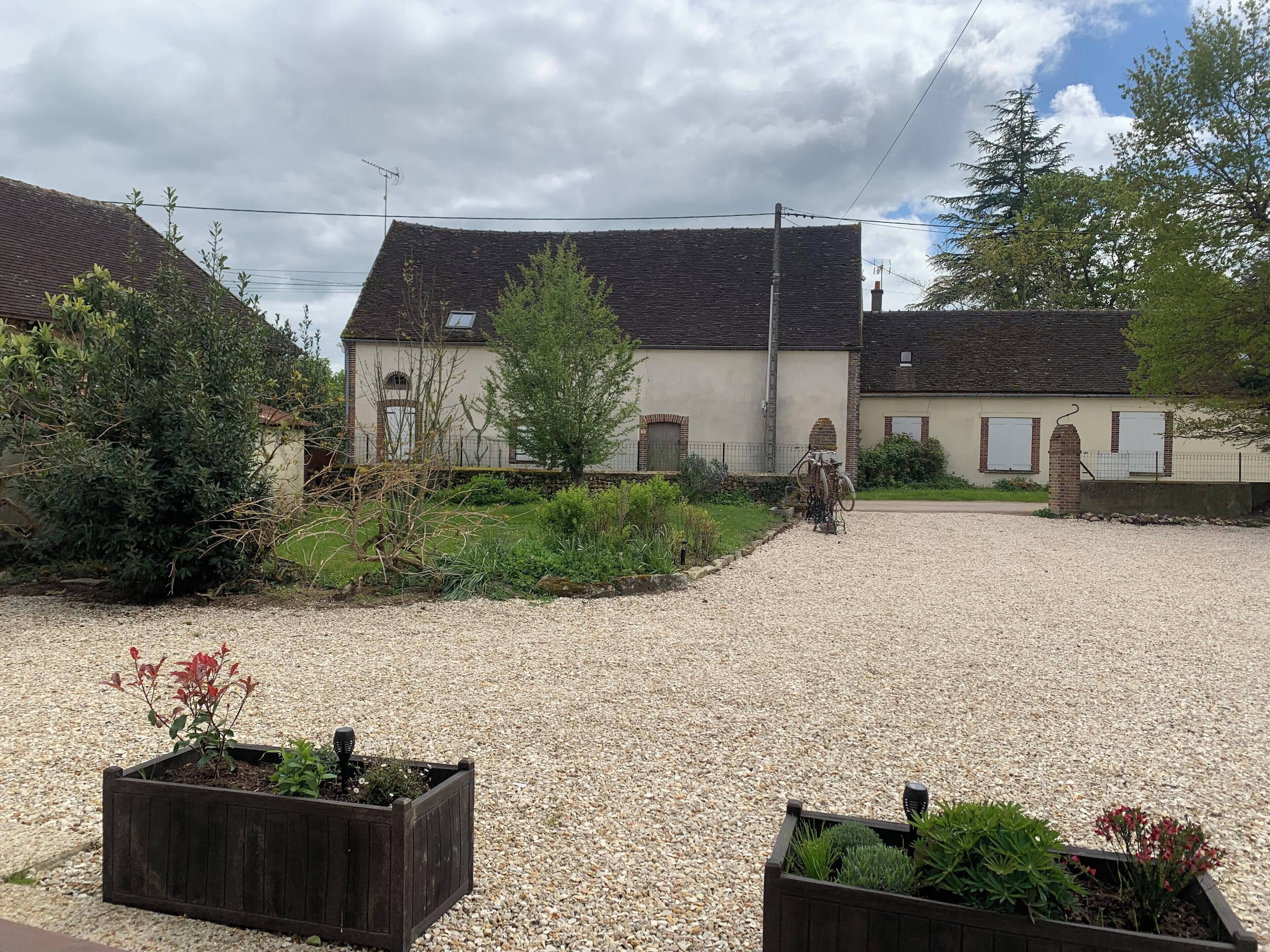 Une maison de campagne avec une allée en gravier et des jardinières en bois.