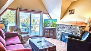 A cozy living room with a fireplace, a large window, and a comfortable seating area. - Top Floor / Heron Point / Hot tub / Pool / AC (Invermere)