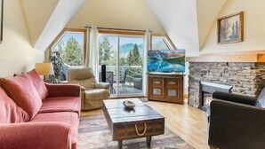 A cozy living room with a sloped ceiling, a fireplace, a sofa, a coffee table, and a television. - Top Floor / Heron Point / Hot tub / Pool / AC (Invermere)