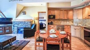 A modern kitchen with wooden cabinets, a dining table set for four, and a stone fireplace. - Top Floor / Heron Point / Hot tub / Pool / AC (Invermere)