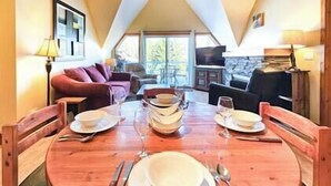 A dining area with a wooden table set for four, a sofa, and a television in the background. - Top Floor / Heron Point / Hot tub / Pool / AC (Invermere)