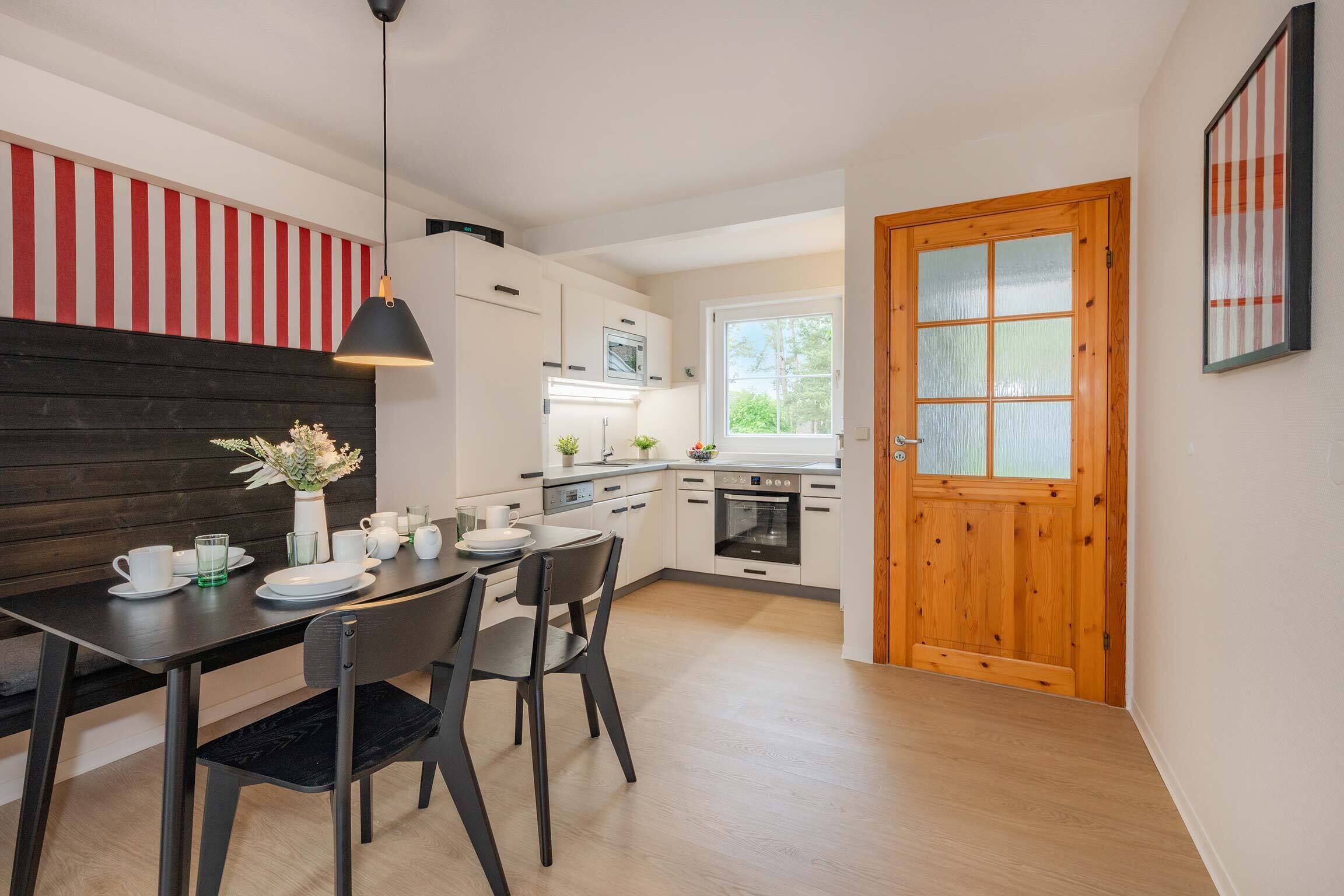 A modern kitchen with white cabinets, a wooden dining table, and a black pendant light.
