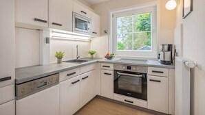 Una cocina moderna con armarios blancos, horno empotrado, microondas y cafetera.