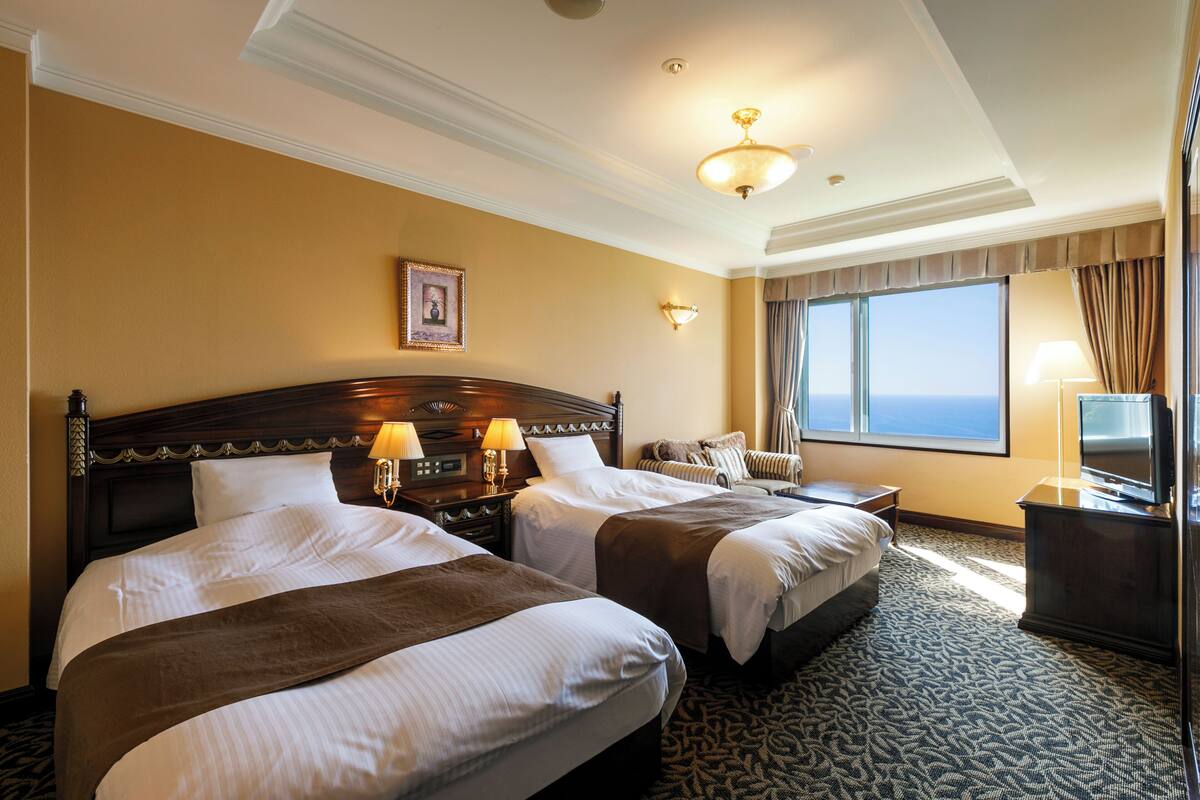 A hotel room with two beds, a large window with a view, and a television on a dresser.