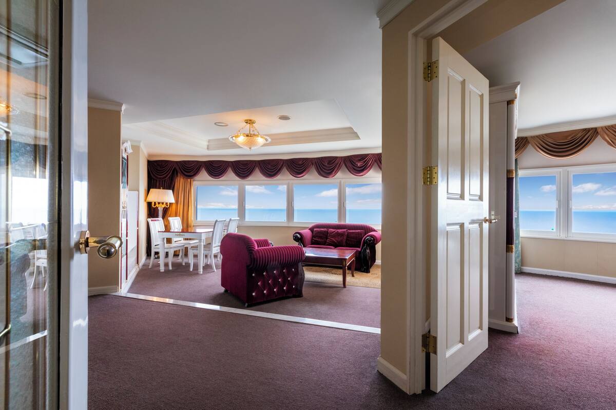 A spacious room with a view of the sea, a dining area with a table and chairs, and two plush armchairs.