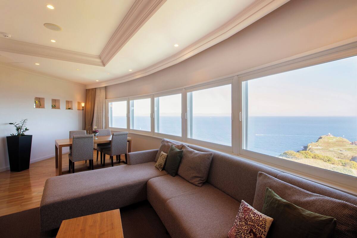 A modern living room with a curved ceiling, a large sofa, a dining area, and a view of the sea.