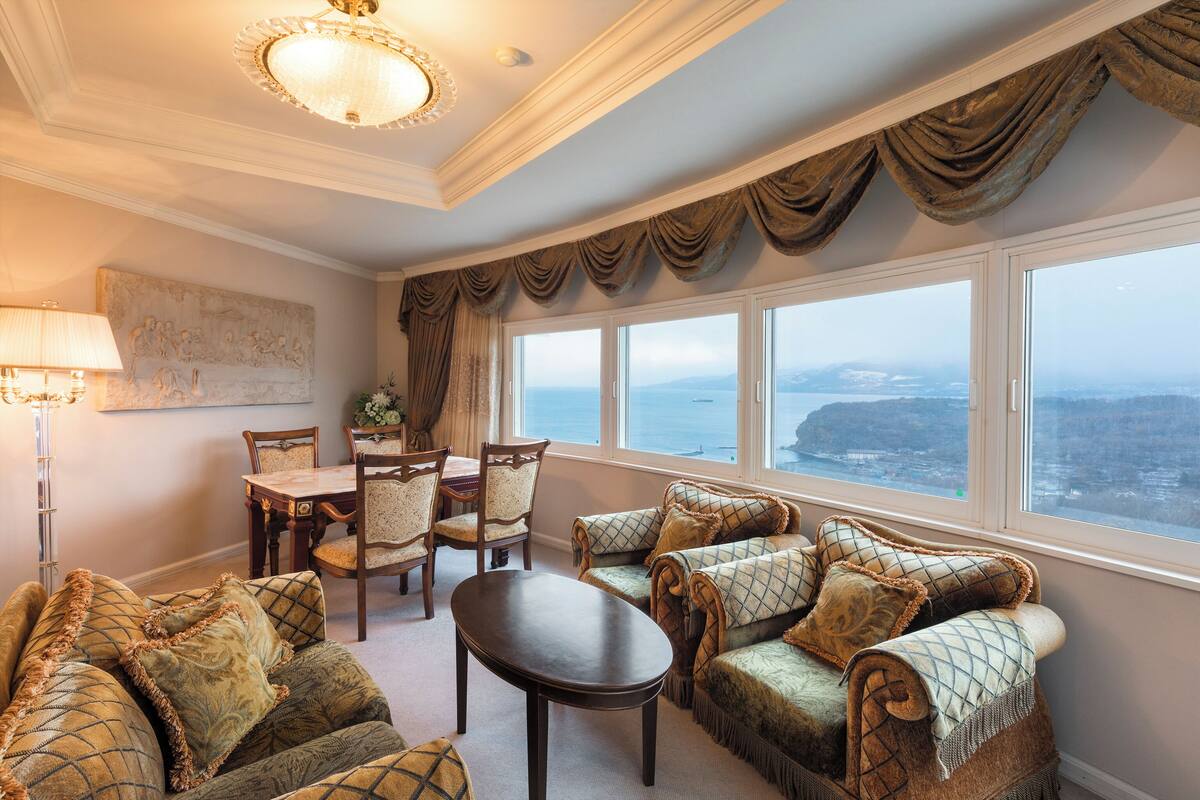 A room with a dining area, a sofa set, and a view of the sea.