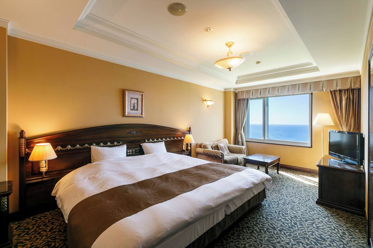 A hotel room with a large bed, a sofa, a TV, and a window with curtains.