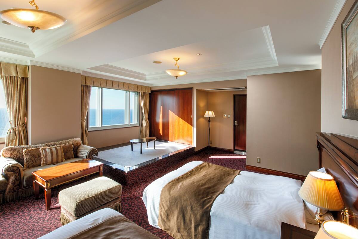 A hotel room with a sofa, two beds, a table, and a lamp.