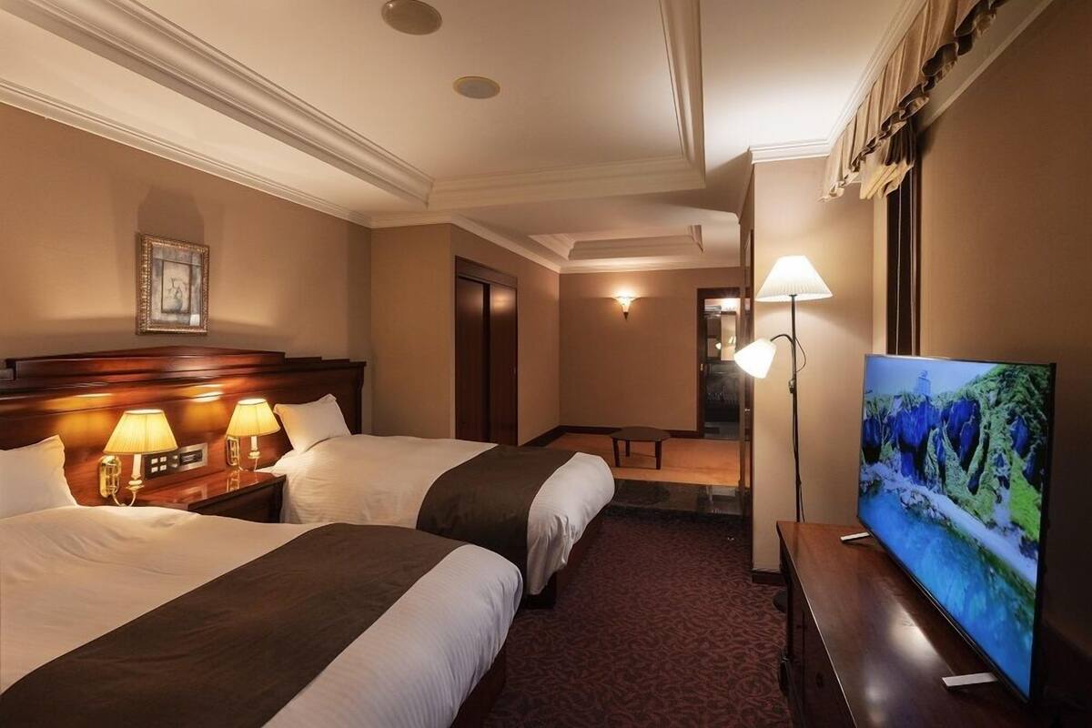 A hotel room with two beds, a television, a desk, and a lamp.