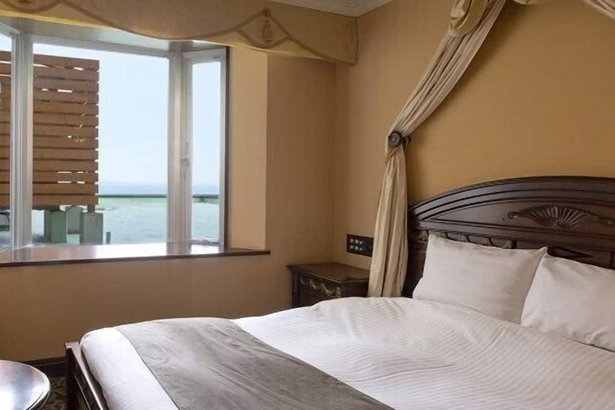 A hotel room with a bed, a nightstand, a window with a view, and a curtain.
