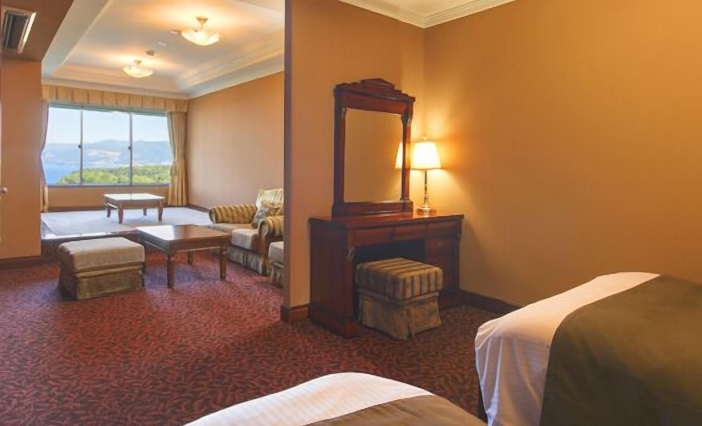 Camera d'albergo con un letto, una scrivania, una sedia, un tavolino, uno specchio e vista sull'esterno.