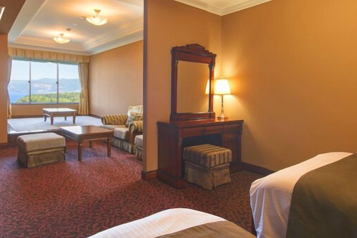 A hotel room with a bed, a desk, a chair, a small table, a mirror, and a view of the outdoors.