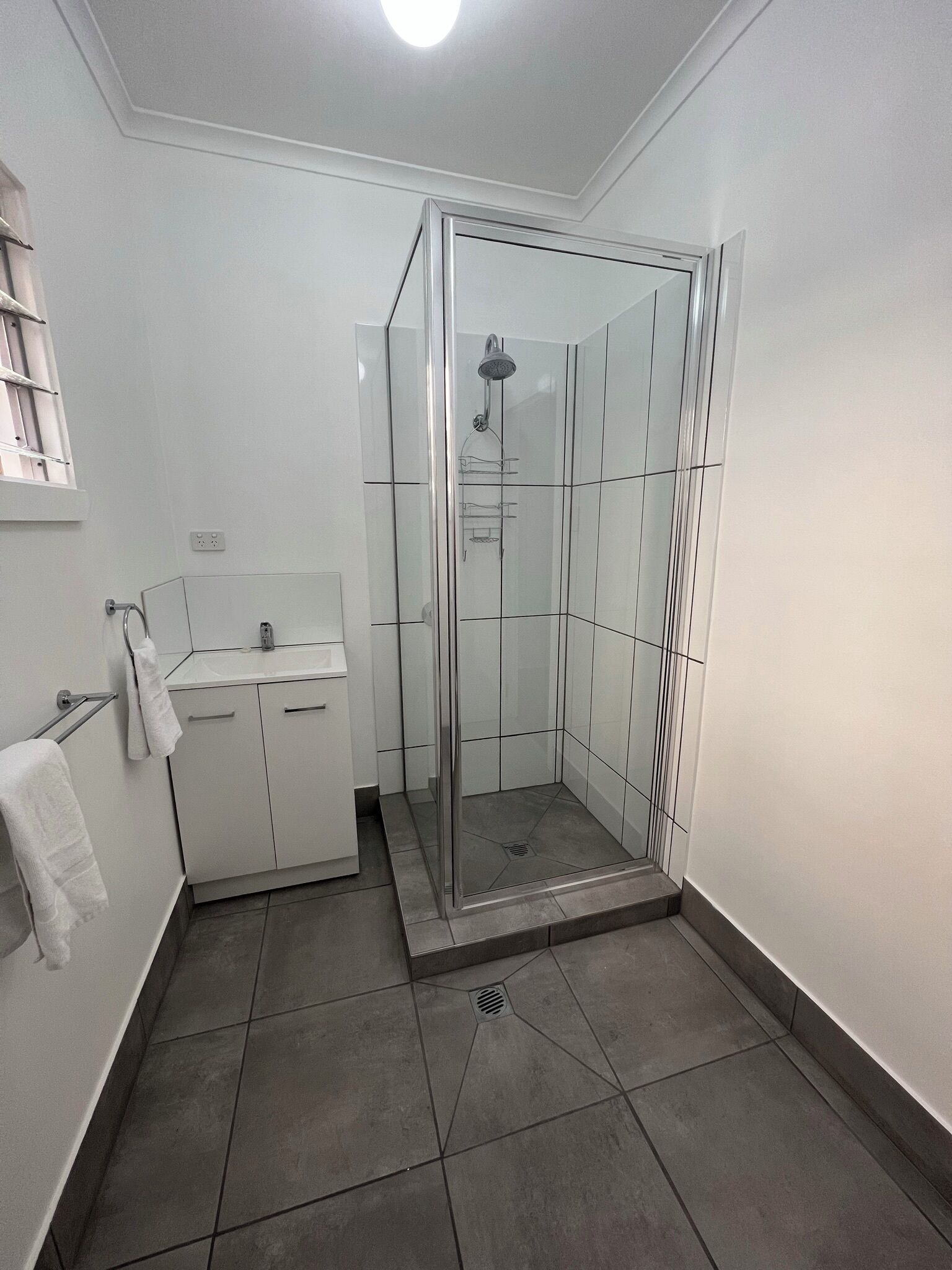 A modern bathroom with a glass shower enclosure, a white sink, and a towel rack.