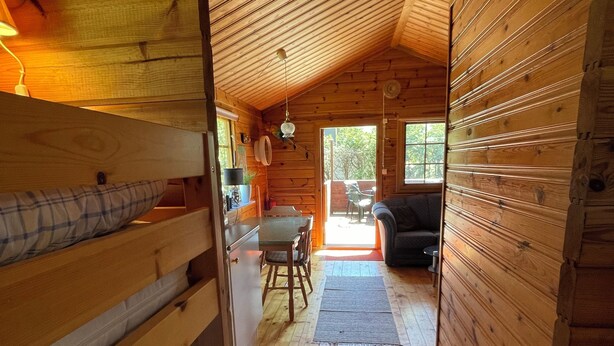 A wooden cabin interior with bunk beds, a dining table, and a sofa.