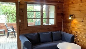 A cozy cabin interior with a dark blue sofa, a white round table, and a window with a view of greenery outside.