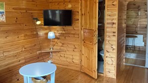 A wooden cabin interior with a television mounted on the wall, a small table with a lamp, and a blue sofa.