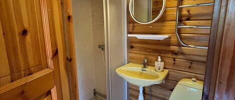 A wooden-paneled bathroom with a shower, a sink, and a toilet.