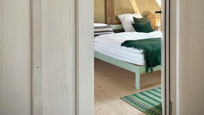A bedroom with a sloped ceiling, a bed with white bedding, a green throw blanket, and a green rug. - 5 Bedroom Agritourism property in Stockach (Stockach)