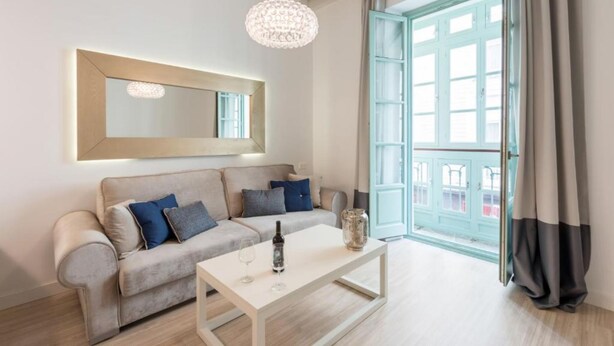 Een moderne woonkamer met een bank, een salontafel, een kroonluchter en een groot raam met gordijnen.