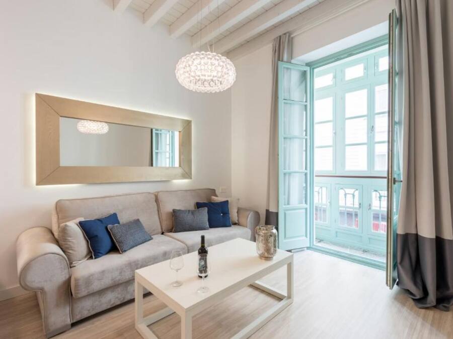 Una sala de estar moderna con un sofá, una mesa de centro, una araña y un gran ventanal con cortinas.