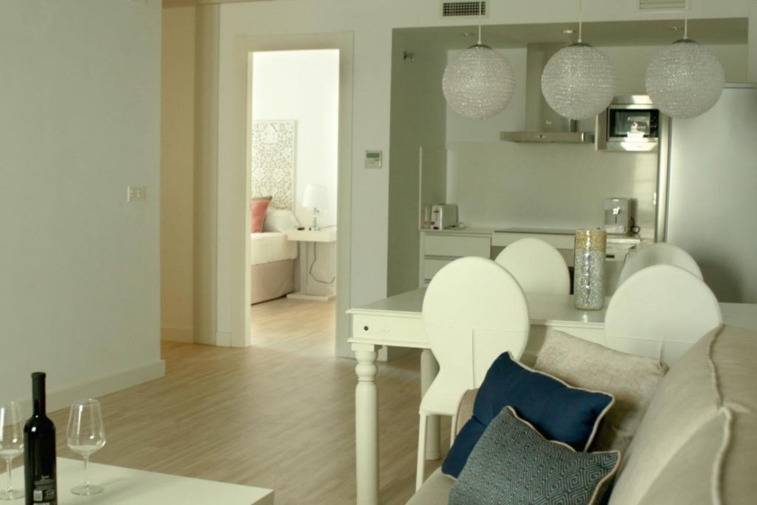 Een moderne woonkamer met een witte bank, een eettafel met stoelen, en een keuken op de achtergrond.