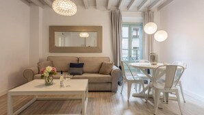 Een moderne woonkamer met een beige bank, een witte salontafel en een eethoek met een ronde tafel en witte stoelen.
