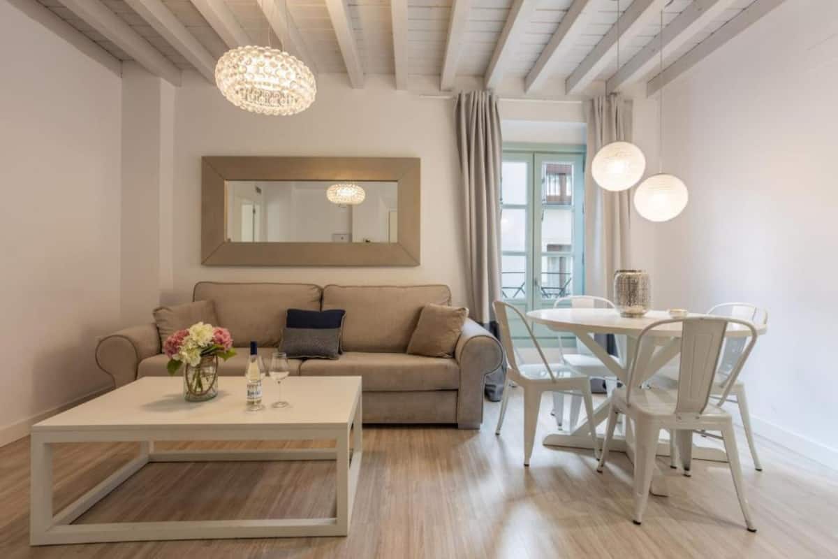 A modern living room with a beige sofa, a white coffee table, and a dining area with a round table and white chairs.