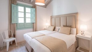 Een kamer met een tweepersoonsbed, een houten hoofdbord, twee nachtkastjes met lampen, een stoel en een raam met gordijnen.