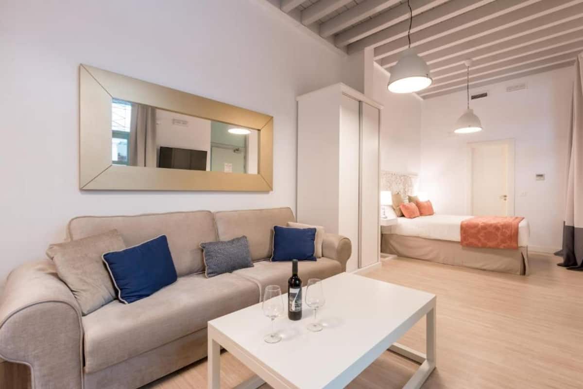 A modern living room with a sofa, a coffee table, and a bed in the background.