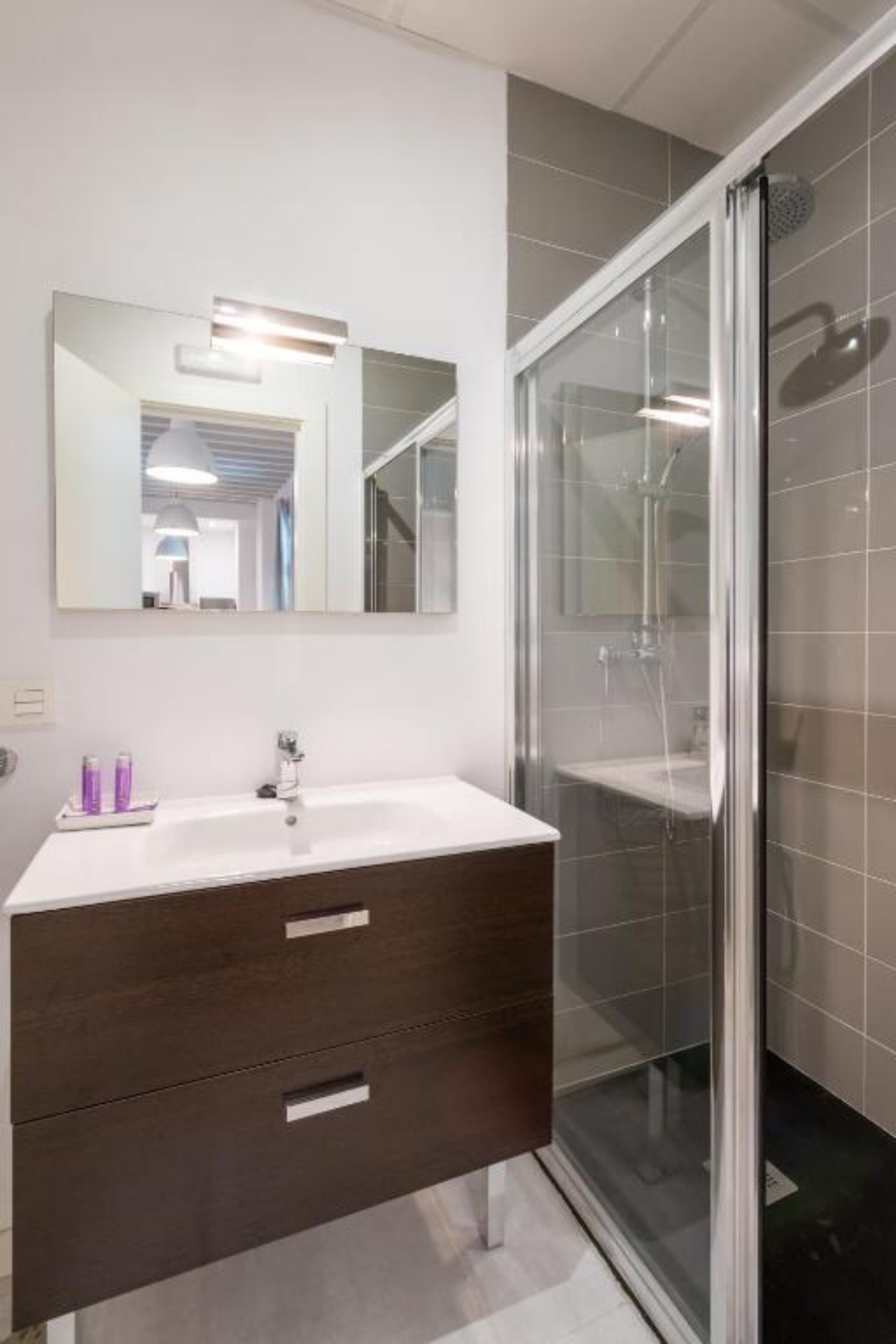 Une salle de bain moderne avec une douche à parois de verre, un lavabo blanc et un meuble-lavabo en bois foncé.