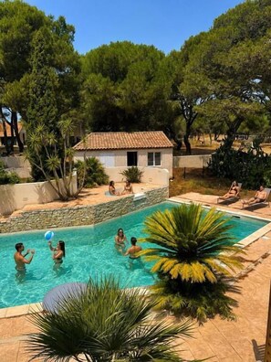 Une piscine avec des personnes, un petit bâtiment et des arbres tout autour.
