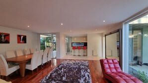 Ein modernes Wohnzimmer mit Essbereich, einem roten Sofa und einer Küche im Hintergrund.