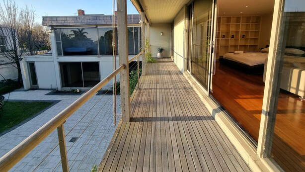 Ein moderner Balkon mit Holzboden, große Schiebeglastüren, die in ein Schlafzimmer mit Bett und Nachttisch führen.