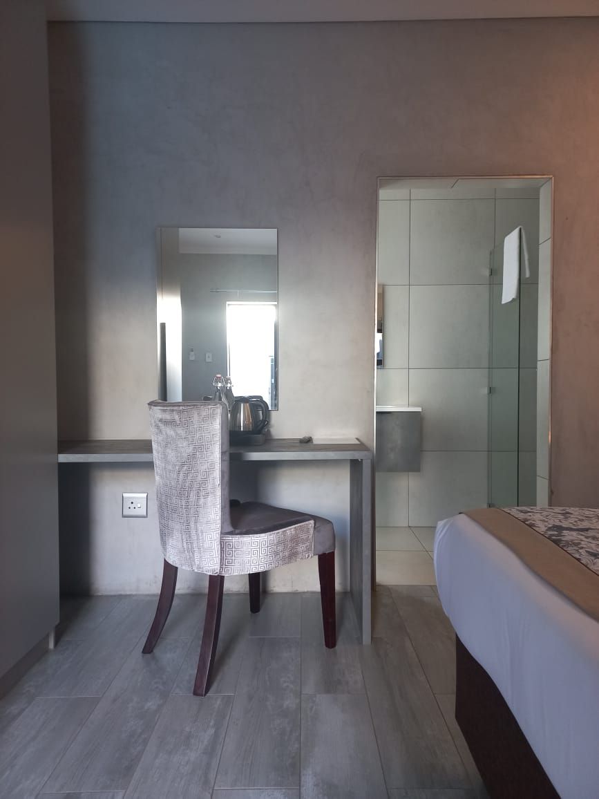 A bedroom with a bed, a desk with a chair, a mirror, and a bathroom with a shower.