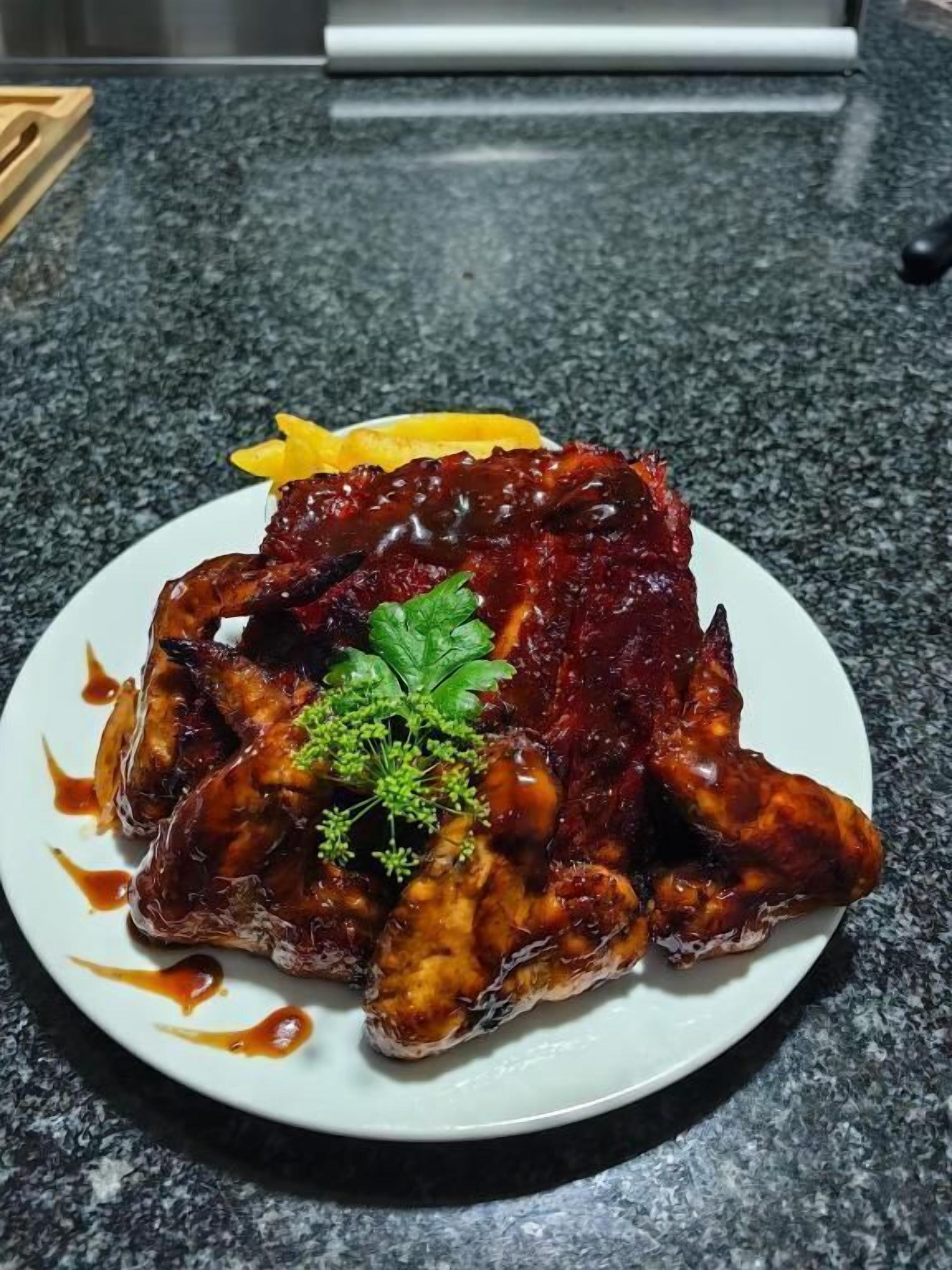 A plate of glazed chicken wings with a garnish of parsley and a lemon wedge on a granite countertop.