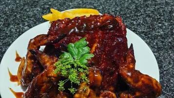 A plate of glazed chicken wings with a garnish of parsley and a lemon wedge on a granite countertop.
