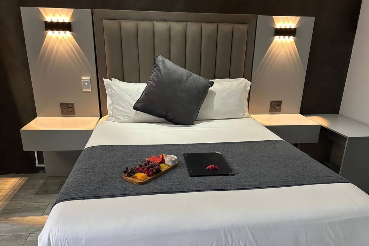 Una habitación de hotel moderna con una cama grande, dos mesitas de noche e iluminación integrada en la pared.