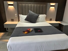 Una habitación de hotel moderna con una cama grande, dos mesitas de noche e iluminación integrada en la pared.