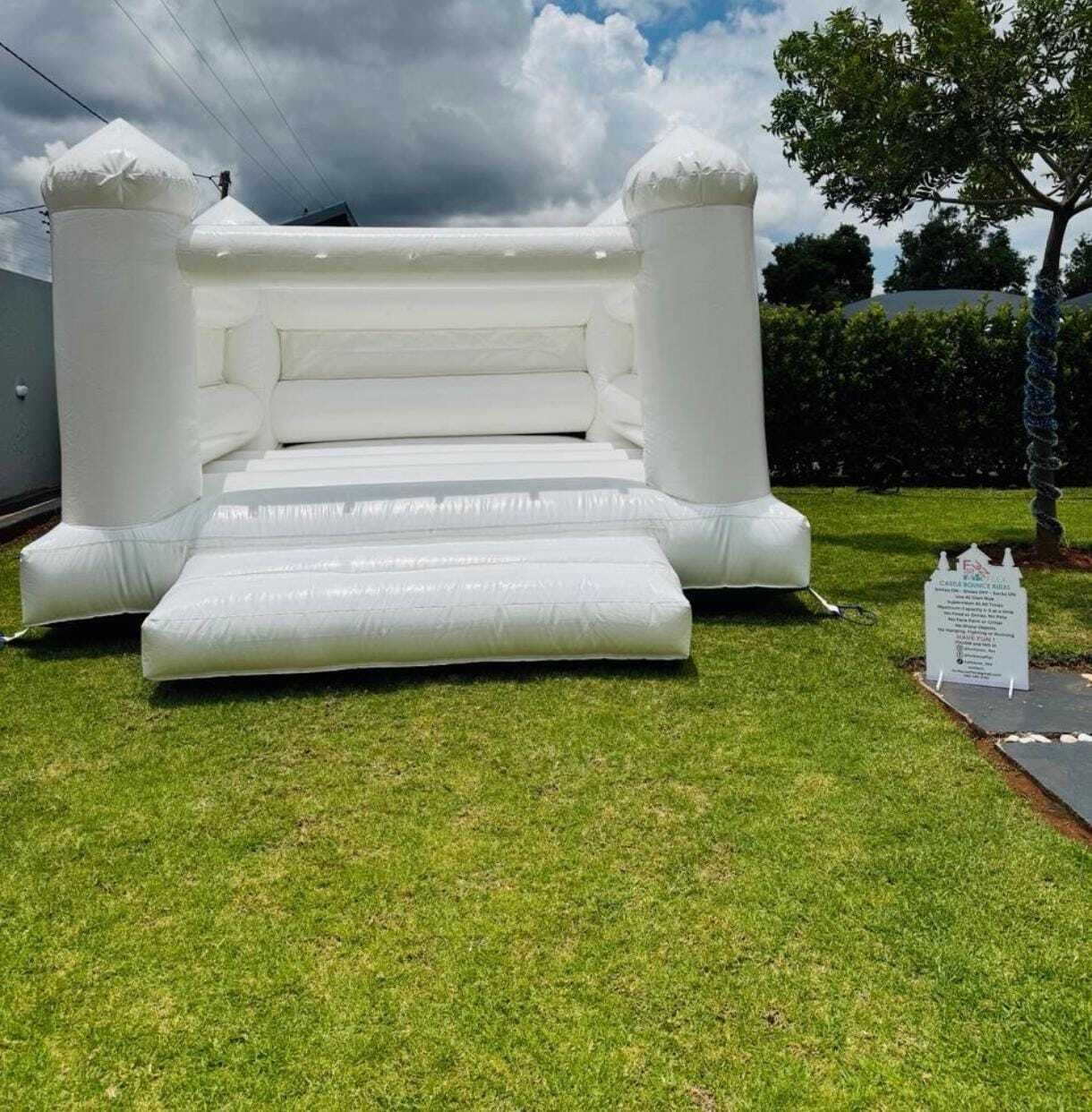 A large inflatable bouncy castle in a grassy area with a sign and trees in the background.